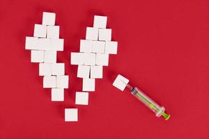 Gebrochenes Herz aus Zuckerwürfeln und einer Spritze auf rotem Hintergrund. Diabetes-Konzept. Sicht von oben. Raum schaffen. foto