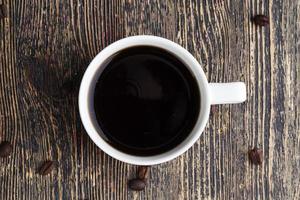 eine weiße Tasse mit einem schwarzen Getränk und Kaffeebohnen foto