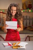 glückliche Hausfrau, die Brief in der weihnachtlich dekorierten Küche liest foto