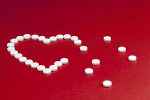 medizinische Tabletten, die auf rotem Hintergrund in Form eines Herzens gestapelt sind foto