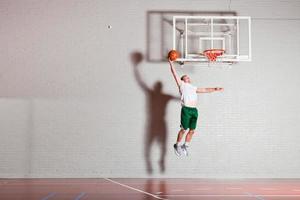 harter gesunder junger Mann, der Basketball in der Turnhalle spielt.
