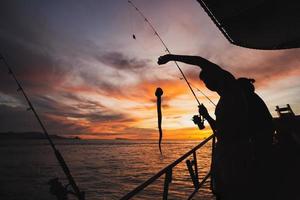 Silhouette junger Mann Angeln im offenen Meer vom Boot aus. foto