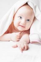 glückliches Baby nach dem Baden, schaut mit weißen Handtüchern, lustiges Lächeln foto