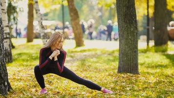 sexy attraktives weibliches blondes Bikini-Fitnessmodel, das sich im Herbstpark auf dem Boden ausdehnt, bedeckte gelbe Blätter - Flexibilität der Beine foto