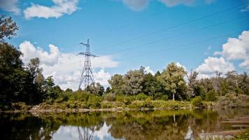 Breitbild-Zeitraffer von Stromleitungen und Hochspannungsmasten auf einem Feld auf dem Land im Sommer in der Nähe des Flusses foto