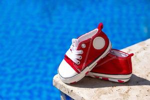 Ein Paar rote Turnschuhe für einen Jungen auf einem Hintergrund aus blauem Wasser im Pool. reisekonzept mit kindern, kindlicher lebensstil. Platz kopieren. foto