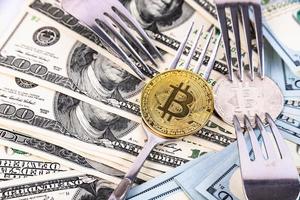 Gold-Bitcoin auf dem Hintergrund von Hundert-Dollar-Scheinen und Besteck. foto