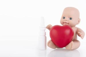 Puppe, Baby, mit einem roten Herz in ihren Händen und einem Nasenspray. Kinderschutzkonzept. Platz kopieren foto