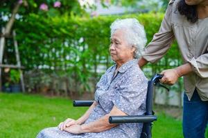 pflegekraft hilft asiatischen älteren frauen mit behinderungspatienten, die im park im rollstuhl sitzen, medizinisches konzept. foto