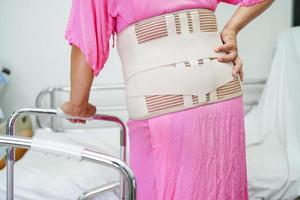 asiatische seniorenschmerzen zurück mit elastischem stützgürtel mit gehhilfe. foto