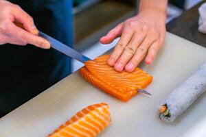 Den Lachs mit einem Messer schneiden, japanischer Koch macht Sashimi in der Küche, Sushi werden gemacht foto