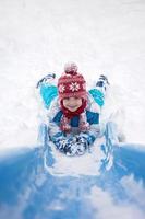 süßer kleiner Junge, der eine schneebedeckte Rutsche hinuntergeht foto