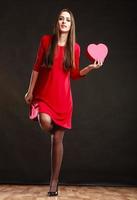 Frau, die Herz im roten Kleid hält.