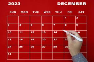 Dezember 2023 Kalender mit Hand, die schwarzen Stift auf rotem Hintergrund hält. foto
