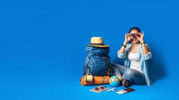 junge asiatische reisende glückliche frau im blauen hemd mit rucksack mit und ausrüstung für reisende urlaub mit einer karte, auf blauem farbhintergrund. Reiserucksack foto