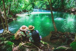 reisende, paare mit rucksäcken, sitzen und entspannen auf den felsen. reise durch die natur im grünen dschungel und genieße die aussicht im wasserfall. Tourismus, Wandern, Naturkunde. Paare reisen, fotografieren foto