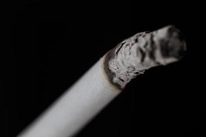 brennende Zigarette mit Rauch auf schwarzem Hintergrund foto