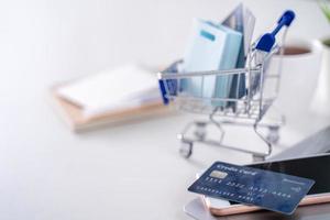 Online-Zahlung im Büro, Einkaufen zu Hause bleiben, elektronische Zahlung mit Kreditkartenkonzept, Laptop auf weißem Tischhintergrund mit Einkaufswagen, Nahaufnahme. foto