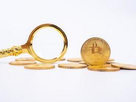 goldene bitcoin-replik und lupe auf weißem hintergrund. geschäfts- und finanzkonzept. foto