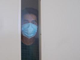 Einsamer Mann in medizinischer Maske, der durch das Fenster schaut. Isolierung zu Hause für Selbstquarantäne. konzept hausquarantäne, prävention covid-19. Ausbruchssituation des Coronavirus foto