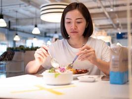 asiatische frau, die getrennt im restaurant sitzt und essen mit einer tischschild-kunststofftrennwand isst, um eine infektion vor coronavirus covid-19 zu schützen foto