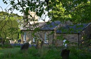 Kippen alter Grabsteine auf einem Friedhof neben einer alten Kirche foto