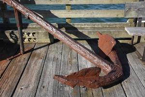 Schwerer verrosteter Bootsanker, der auf einem Holzsteg ruht foto