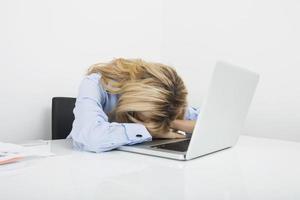 müde Geschäftsfrau, die Kopf auf Laptop am Schreibtisch ausruht foto