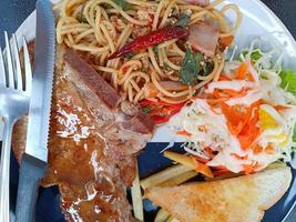 Draufsicht, Spaghetti mit würzigem Schweinefleisch und Schweinekotelett, serviert mit Gemüsesalat und Toastbrot foto