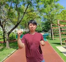 Glücklicher asiatischer junger Mann, der im Sommer im Stadtpark joggt foto