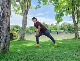 junger asiatischer mann mit brille und dunklem haar, der yoga macht oder sich unter einem baum aufwärmt. in der Sommerparkstadt foto