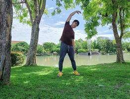 junger asiatischer mann mit brille und dunklem haar, der yoga macht oder sich unter einem baum aufwärmt. glücklich und entspannt. in der Sommerparkstadt foto