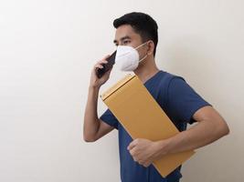 glücklicher lieferdienstmitarbeiter in medizinischer gesichtsmaske trägt pappkarton in der hand foto