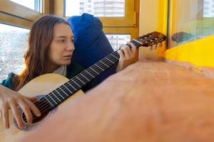 Junge Frau spielt klassische Gitarre auf dem Balkon foto