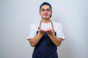 junger asiatischer barkeeper mit schürze, die seine leere handfläche nach vorne zeigt und etwas hält foto