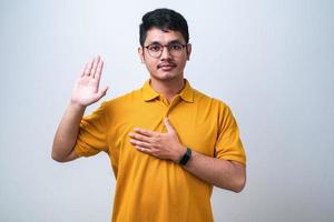 junger gutaussehender mann, der mit der hand auf der brust und offener handfläche schwört und einen treueschwur leistet foto