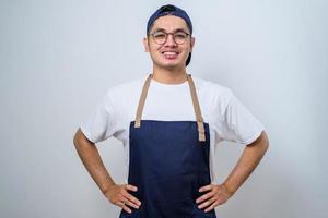 junger asiatischer barista-mann mit schürze, der mit den händen auf der taille steht foto