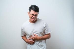 junger gutaussehender asiatischer mann mit lässigem hemd und brille, der bauchschmerzen bekommt oder bauchschmerzen bekommt gesundheitsprobleme beschwerden durchfall foto
