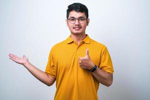 asiatischer mann, der ein lässiges hemd trägt, das eine handfläche zeigt und eine ok-geste mit erhobenen daumen macht, glücklich und fröhlich lächelt foto