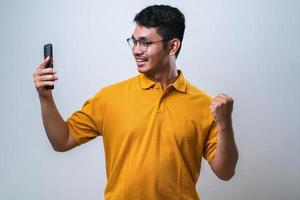 erwachsener asiatischer mann, der glückliche geste zeigt, während er auf sein handy schaut foto