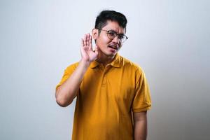 asiatischer Mann, der mit der Hand über dem Ohr lächelt und Gerüchten oder Klatsch zuhört. Taubheitskonzept. foto
