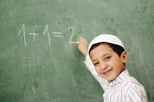 arabisches muslimisches Kind, das auf Tafel im Klassenzimmer schreibt, Mathe foto