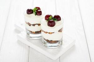 Dessert mit Käse, frischen Kirschen und Müsli in einem Glas auf weißem Holzhintergrund. foto