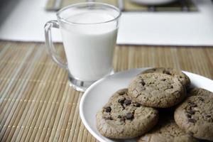 ein glas mit milch auf einer holzmatte mit haferkeksen. Nachmittagsmittagessen mit Plätzchen. süße Kekse mit Milch. foto