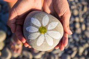 Kiesel mit einem bemalten Gänseblümchen in den Händen eines Kindes auf dem Hintergrund eines Kiesstrandes foto