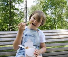 Ein junges Mädchen, das an einem Sommertag im Park spazieren geht, isst mit Nudeln Wok zu Mittag foto