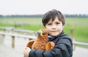 Fröhlicher kleiner Junge, der an einem sonnigen Morgen mit Vogelspielzeug im Park spielt, Kind, das auf Frühlingsfeldern steht, positives Kind mit lächelndem Gesicht, das sich entspannt oder im Sommer Spaß im Freien hat foto