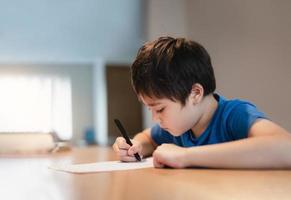 schulkind, das schwarze stiftzeichnung verwendet oder den brief auf papier schreibt, kleiner junge, der hausaufgaben macht, kind mit stift, der während des unterrichts notizen in papierblatt schreibt. süßer schüler, der test macht, homeschooling-konzept foto