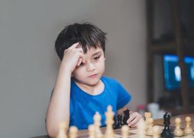 konzentrierter kleiner junge, der schachstrategie entwickelt, brettspiel mit eltern zu hause spielt. aktivität oder hobby für familienkonzept foto