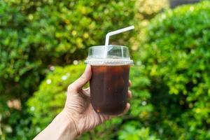 Hand, die schwarzen Eiskaffee oder Americano-Kaffee hält foto